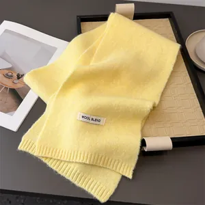 Detailansicht eines weichen, gelben Strickschals aus Wollmischung auf einem Tablett.