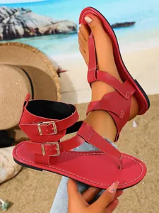 Detailansicht roter flacher Zehentrenner-Sandalen mit Doppelschnallen am Strand
