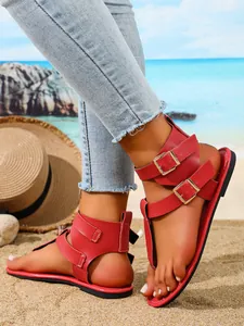 Modische rote flache Zehensandalen mit doppelter Schnalle auf sandigem Strandhintergrund.
