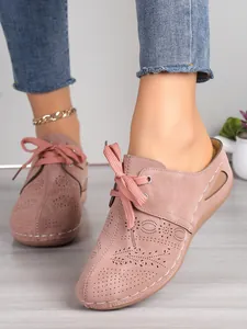 Vue détaillée de mules à talons compensés rose poudré avec motifs floraux découpés au laser.
