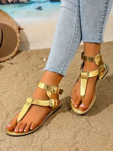 Detailaufnahme goldener Damen-Flachsandalen mit Doppelriemchen am sonnigen Strand