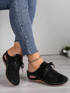 Gros plan de mules compensées noires à bout fermé avec lacets et découpes.