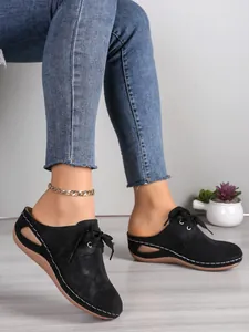 Vue latérale de mules compensées à bout fermé en daim noir avec découpes et coutures blanches
