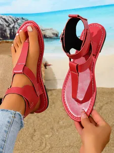 Trendige rote T-Steg-Flachsandalen mit doppelten Schnallen an einem hellen Sommerstrand.