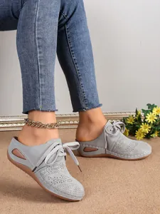 Gros plan de mules compensées grises découpées au laser avec lacets portées par un mannequin