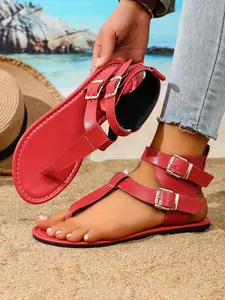 Trendige rote flache Zehentrenner-Sandalen für Damen mit Doppelbuckle am Strand.