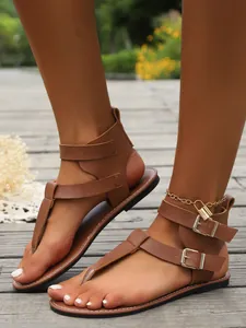 Detail von braunen flachen Zehenstegsandalen mit doppelten Schnallenriemen und Fußkettchen.