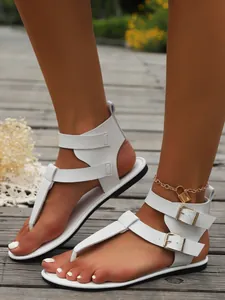 Detailaufnahme weißer flacher Zehentrenner-Sandalen mit doppelten Schnallenverschlüssen.