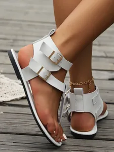 Detailaufnahme weißer flacher Sandalen mit doppelten goldenen Schnallen und Riemen