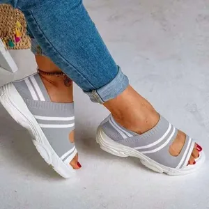 Bequeme graue Keilsandalen aus Strick mit weißen Streifen am Fuß einer Frau