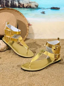 Detail von goldenen Metallic-Flachsandalen mit Doppel-Schnallenriemen am Sandstrand