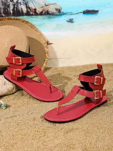 Detailansicht roter flacher Zehensandalen mit doppelten Gold-Schnallen am Strand.