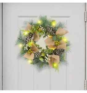 Detail eines leuchtenden Weihnachtskranzes mit Zapfen und Leinenschleifen an weißer Tür