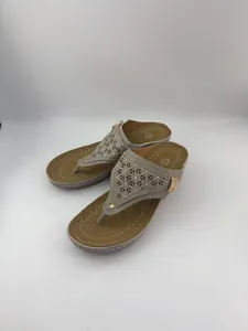 Dettaglio di sandali infradito grigi con zeppa e motivi floreali intagliati laser.