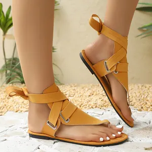 Detailansicht der senfgelben flachen Gladiatorensandalen mit Knöchelriemen und Metallringen.