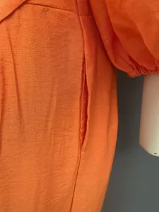 Close-up detail of a bright orange textured fabric jumpsuit showing functional side pocket