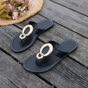 Elegant black flip-flop sandals with a large gold interlocking buckle on a wooden deck