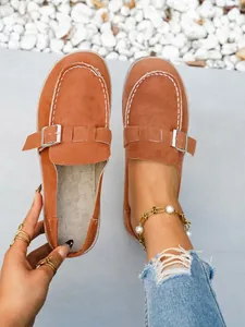 Close-up view of brown faux suede mule slippers with a silver metal buckle detail.