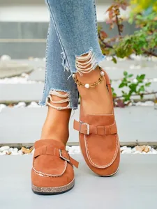 Close-up view of stylish tan suede closed-toe clogs with adjustable metal buckle detail.