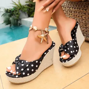 Primer plano de sandalias de cuña elegantes con lunares, suela de paja y detalle de lazo