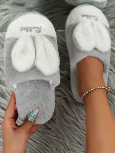 Close-up detail of grey and white plush rabbit ear indoor slippers on a fuzzy rug