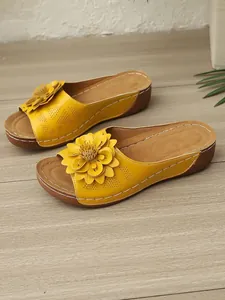 Detailansicht gelber Keilsandaletten mit 3D-Blumen und lasergeschnittenen Mustern.