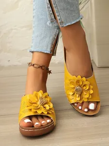 Nahaufnahme gelber Keilsandalen mit großer Zierblume und perforiertem Obermaterial.