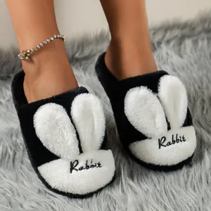 Close-up detail of cute black and white plush rabbit head slippers on a soft gray rug
