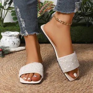Dettaglio di ciabatte piatte bianche con eleganti perle e strass su un tappeto di paglia
