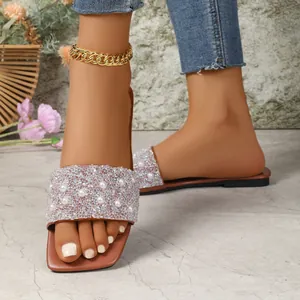 Primo piano di sandali piatti da donna con eleganti perle e cinturini in strass.