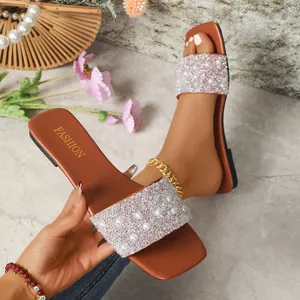 Dettaglio di eleganti ciabatte basse marroni con perle e strass luccicanti sulla fascia