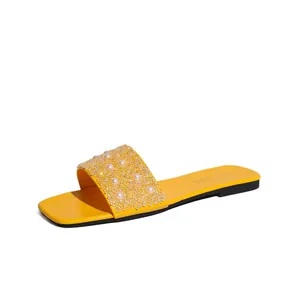 Dettaglio di ciabatte piatte gialle con strass scintillanti e decorazione di perle eleganti.