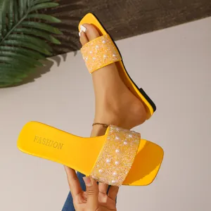 Primo piano di ciabatte gialle a punta quadrata con eleganti perle e dettagli in strass.