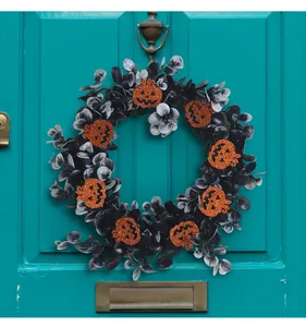 Halloween wreath with black eucalyptus leaves and glittery orange pumpkins on teal door