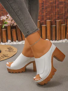 Detail view of white peep-toe platform mules with chunky brown heels worn on feet.