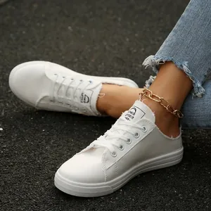 Detailopname van witte canvas instapsneakers met rafelranden en gouden enkelbandje.