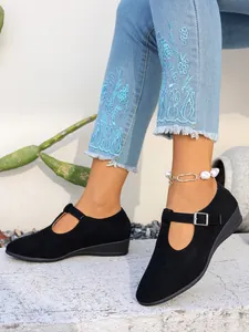 Dettaglio di scarpe zeppa in camoscio nero con cinturino a fibbia e jeans ricamati