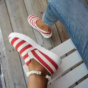 Close-up van comfortabele rood en wit gestreepte canvas instappers voor dames op een houten dek.