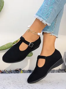 Dettaglio scarpe nere in pelle scamosciata con cinturino a T e comoda suola a zeppa