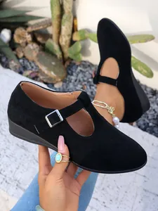 Dettaglio delle scarpe con zeppa in pelle scamosciata nera e cinturino con fibbia argento