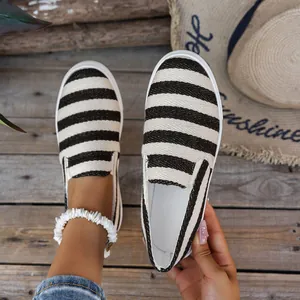 Detailweergave van zwart-wit gestreepte canvas loafers op een houten achtergrond.