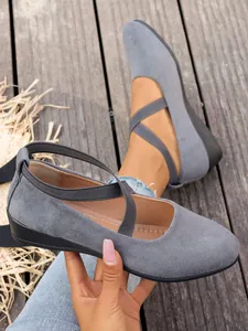 Eleganti ballerine in pelle scamosciata grigia con cinturini elastici incrociati su legno