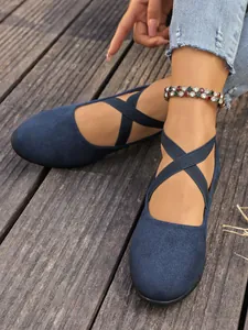 Eleganti scarpe basse in camoscio blu scuro con cinturini elastici incrociati su legno.