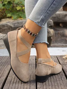 Primo piano di scarpe scamosciate beige da donna con cinturini elastici incrociati.
