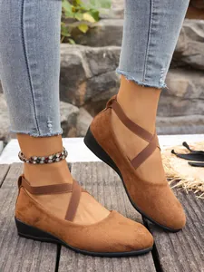 Dettaglio di scarpe con zeppa in camoscio marrone e cinturini elastici incrociati