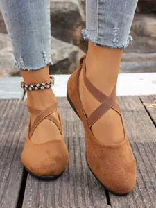 Dettaglio ballerine in camoscio marrone con cinturini elastici incrociati su legno