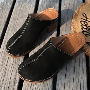 Vue détaillée de mules en daim noir avec surpiqûres blanches et talons épais façon bois.
