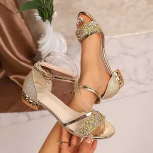 Detailansicht goldener Sandalen mit Strasssteinen, Blockabsatz und elegantem Riemen.