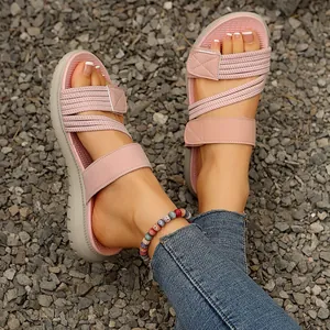 Primer plano de sandalias de cuña rosas con velcro y bandas elásticas sobre grava