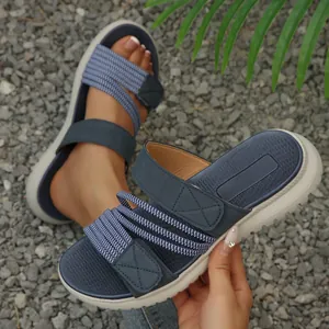 Sandalias de verano azules con correas cruzadas y cierre de velcro sobre fondo de grava